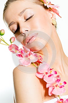 Closeup on beautiful young lady with perfect skin, closed eyes and luxury jewelry earring holding orchid flower