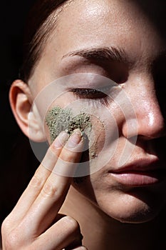 Closeup of Beautiful Young Woman with organic cosmetic mask scrub touch own face. Black background