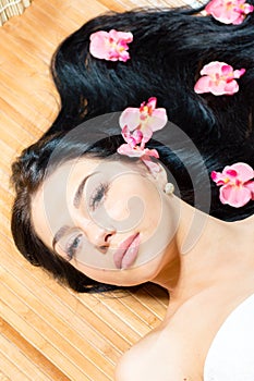 Closeup on beautiful young woman with perfect skin, blue eyes, luxury jewelry earring and orchid flowers looking at camera