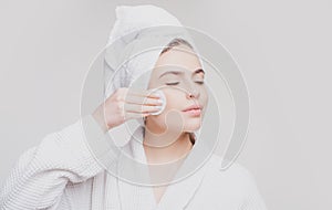 Closeup of Beautiful Young Woman washing her face with the Cotton Pad on the gray background. Eyes are Closed.