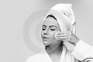 Closeup of Beautiful Young Woman washing her face with the Cotton Pad on the gray background. Eyes are Closed.