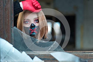 Closeup beauty portrait of a beautiful girl in a black mask with rhinestones, makeup designer. Looking out from a broken window.