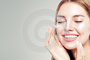 Closeup beauty portrait of laughing woman with healthy skin applying cosmetic cream on her face.