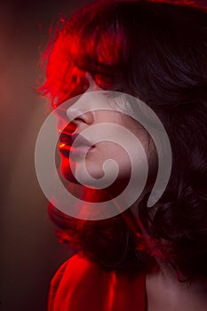 Closeup beauty portrait of young woman with makeup and hairstyle, wear red suit, with closed eyes, red studio light.