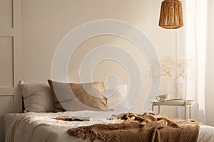 Closeup of bed with beige blanket and linen pillow in minimal bedroom interior, real photo