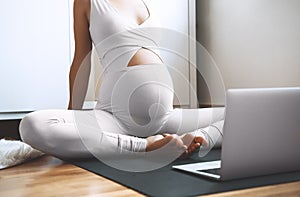 Closeup belly of pregnant woman practicing yoga online with laptop