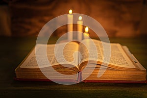 closeup of a bible with three candles out of focus in the background