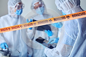 Closeup of biohazard tape blocking of prohibited area. Team of scientists cleaning prohibited area. Medical csi team