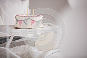 Closeup of birthday cake with candles on wooden tray in the middle of king size bed