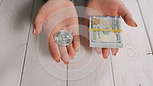 Closeup of a bitcoin and a stack of hundred dollar bills in the hands of a woman