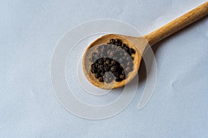 Closeup black pepper seeds or peppercorns  dried seeds of piper nigrum in wooden spoon isolated on white background. top view.