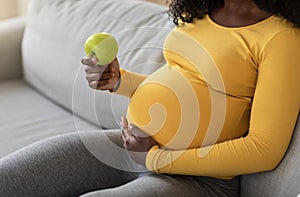 Closeup of black pregnant woman holding green apple
