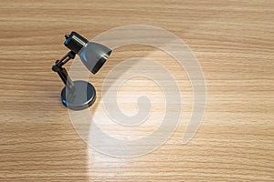 Closeup black small lamp with light in the dark room on wood desk textured background with copy space