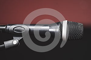 Closeup black vocal microphone mounted on mic stand, blurry red dark bcakground