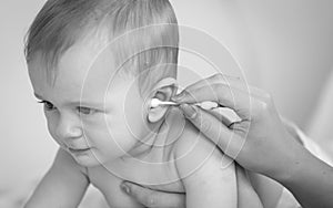Closeup black and white photo of mother cleaning her baby`s ears with cottong swab