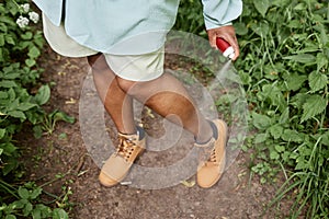 Closeup of black woman spaying legs with bug repellent while travelling