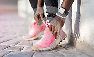 Closeup of black womans hands tying the laces of her running shoes, getting ready for a jog on the road.
