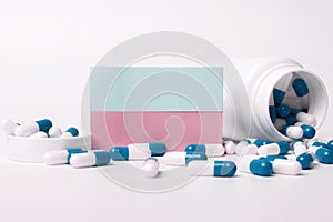 Closeup of a blank blue and pink sticky note and blue-white pills spilling out of pill bottle. Medical concept. Blank space for