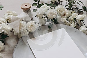 Closeup of blank greeting card. Moody wedding table mockup scene. Feminine desktop composition with fading white rose