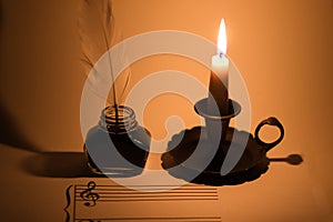 Closeup of a blank music sheet with a vintage ink pot and a lit candle