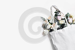 Closeup of blank shopping canvas tote bag mockup with pink tulips, daffodils flowers and eucalyptus isolated on white photo