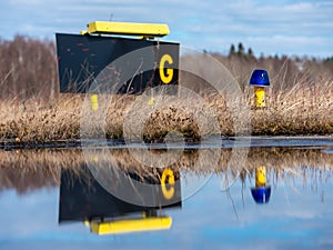 Closeup of a blue airport taxiway light with taxiway G sign in the background. Reflection on the water