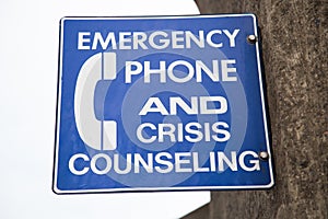 Closeup of a blue [Emergency Phone And Crisis Counseling] sign on a wall with a blurry background