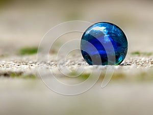Closeup of a blue glass marble taking from the side with blurred background