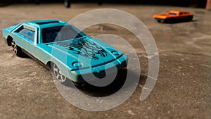 Closeup of blue toy car for children on diverse background with orange toy car on background.