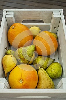 A closeup of a blue wooden box filled with grapefruit, pears of various kinds fresh in season on acacia wood background