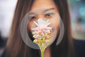 Closeup blur image of a beautiful Asian woman looking at a pink Siam Tulip flower