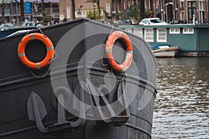 Closeup of a boat with orange lifebuoys in the canal against the Amsterdam cityscape