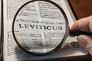 closeup of the book of Leviticus from Bible or Torah using a magnifying glass to enlarge print.