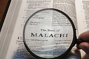 closeup of the book of Malachi from Bible or Torah using a magnifying glass to enlarge print.