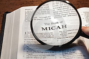 closeup of the book of Micah from Bible or Torah using a magnifying glass to enlarge print.