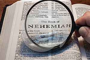 closeup of the book of Nehemiah from Bible or Torah using a magnifying glass to enlarge print.