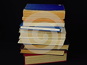 Closeup of books pile. A pile of old books is pictured against dark black background. Old books stacked in a pile.