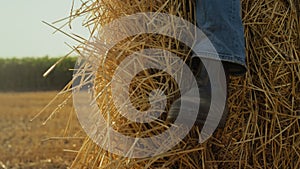 Closeup boot hay stack at wheat stubble field. Farmer resting at straw bale