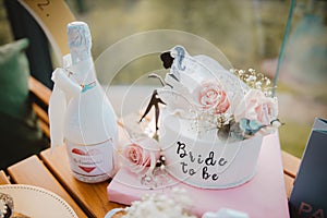 Closeup of a bottle of champagne and a cake decorated with pink roses for 'bride to be' party