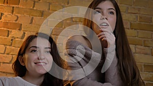 Closeup bottom up portrait of two young pretty women watching TV with excitement in a cozy apartment indoors