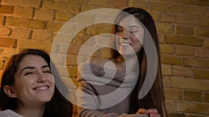 Closeup bottom up portrait of two young pretty women watching TV laughing happily in a cozy apartment indoors