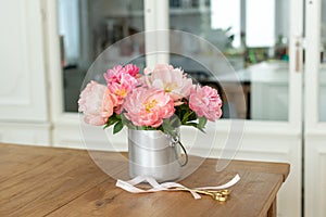Closeup of a bouquet of pink peonies in a metal vase on the table with scissors and a ribbon on it