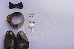 Closeup of bow-tie, belt, shoes, floral corsage, golden rings.