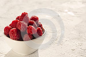 Closeup of bowl of fresh and ripe rasberries on the white surface