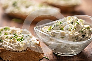 Closeup of a bowl of homemade cream cheese spread with chopped chives surrounded by bread slices with spread and a bunch