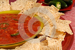 A closeup of a bowl of salsa with tortilla chips and jalapeno pe