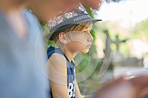 Closeup of a boy with a hat standing in greenery and looking sad because of problems