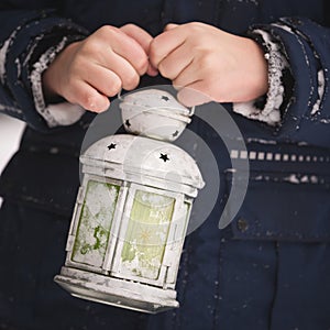 Closeup of a boy`s hand holding a Christmas lantern on a cold winter day. A little boy on the street shines a lantern