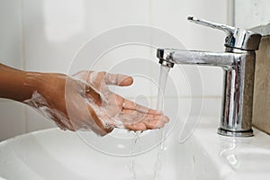 Closeup of a boy scrubbing soapy hand against washbasin