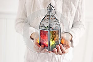 Closeup of boys hands in white tunic shirt holding glowing old Moroccan lantern. Festive greeting card, invitation for